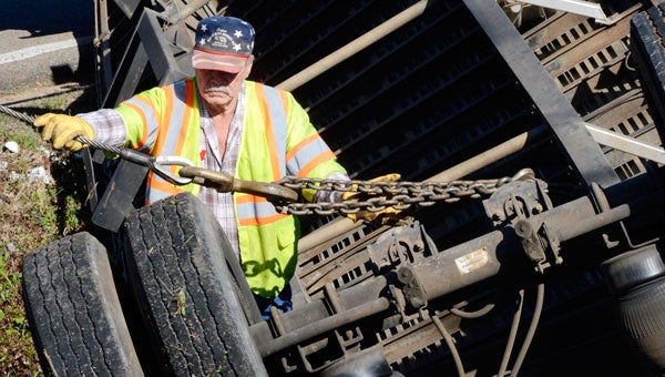 Bruce Carswell attaches a chain from his tow truck to the underside of an overturned tractor trailer Friday morning. (Jay Sowers | Times-Journal)