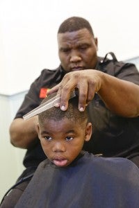 Kairaba Tyus cuts Marquell Davis’ hair Tuesday at the Edmundite Missions’ Slice of Hope back-to-school party. 