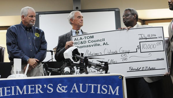 State Senator Hank Sanders presents Oscar Wayne Calloway, AOG director, with a $10,000 check from ALA-TOM RC&D on Monday.  AOG donated a drone to the Dallas County Sheriff’s Department to locate missing persons suffering from Alzheimer's or autism.  Also pictured is Sheriff Harris Huffman Jr.